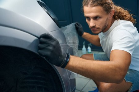 Photo for Young man is gluing anti-gravel film onto the body of a car, he works wearing protective gloves - Royalty Free Image