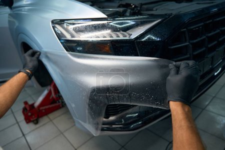 Photo for Man is applying anti-gravel film to the body of a car, the car is standing on a jack - Royalty Free Image