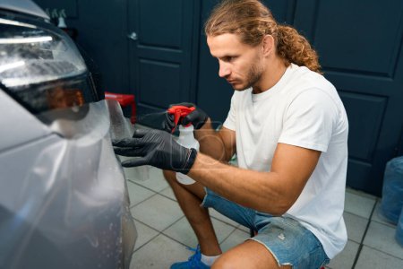 Photo for Male applies anti-gravel film to the car body, he uses a spray bottle - Royalty Free Image