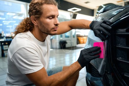 Photo for Man uses pink spatula to apply anti-gravel film to a car body, there are drops of water on the film - Royalty Free Image