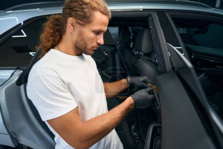 Photo for Young master in protective gloves dismantles a car part, a guy works in a car repair shop - Royalty Free Image