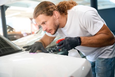 Photo for Specialist applies special clay to scratches on the car body, using a spray bottle - Royalty Free Image