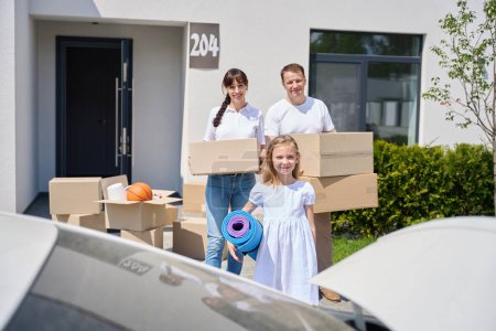Photo for Couple carries boxes of things from the car, their teenage daughter helps them - Royalty Free Image