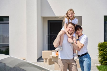 Foto de Alegre familia en el patio de una nueva casa, papá puso a su hija en su cuello - Imagen libre de derechos