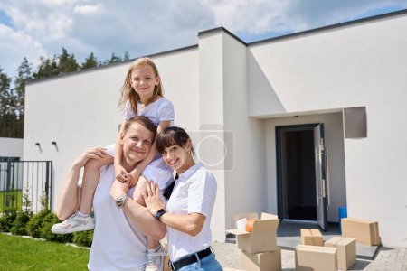 Téléchargez les photos : Joyeux couple avec leur fille dans la cour d'une nouvelle maison, papa a mis la fille sur son cou - en image libre de droit