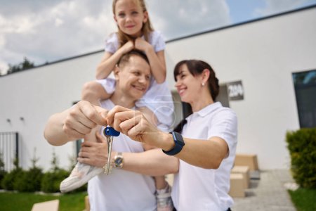 Photo for Happy spouses in the yard with the keys to the new house, the daughter sits on her dads shoulders - Royalty Free Image