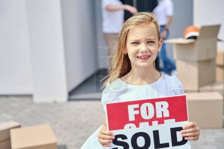 Photo for Cute girl stands in the yard with signs for sale, sold, around a box with things - Royalty Free Image