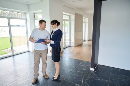 Photo for Man signs documents for buying a house, next to a smiling woman realtor - Royalty Free Image