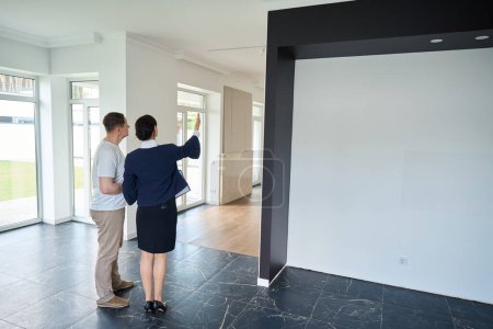 Photo for Client manager shows the house to the buyer, the room is bright and empty - Royalty Free Image