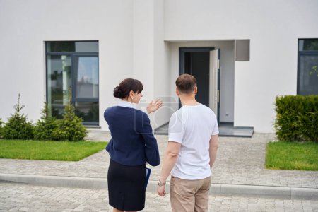 Téléchargez les photos : Acheteur et une femme agent immobilier inspectent l'extérieur d'une nouvelle maison, aménagement paysager dans la cour - en image libre de droit