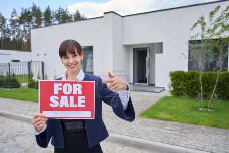 Photo for Realtor lady holds a for sale sign in her hands, a woman in a business suit - Royalty Free Image