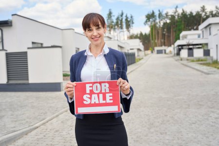 Photo for Lady in a business suit has a for sale sign in her hands, the woman is standing on the street - Royalty Free Image