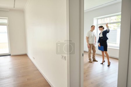 Photo for Buyer, together with a woman realtor, inspects the new house, the room is spacious and bright - Royalty Free Image