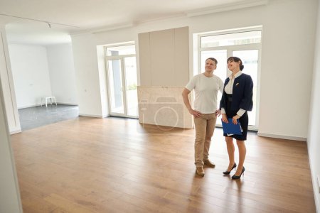 Téléchargez les photos : Femme agent immobilier présente un client à une nouvelle maison, la chambre est spacieuse et lumineuse - en image libre de droit