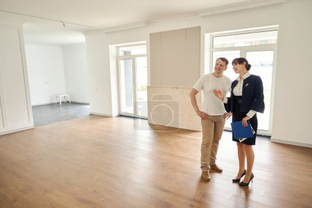 Photo for Female client manager introduces a client to a new house, the room is spacious and bright - Royalty Free Image