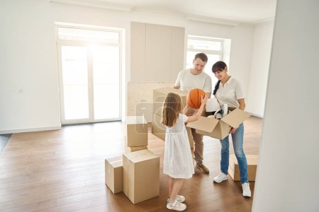 Photo for People unpack things in a new house, a girl takes a ball out of a box - Royalty Free Image