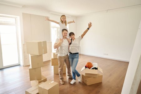 Photo for Happy family in the middle of a spacious empty room, a girl on her dads shoulders - Royalty Free Image
