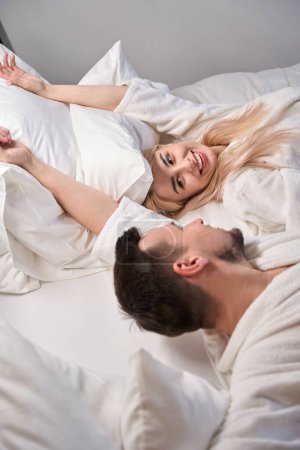 Téléchargez les photos : Joyeux jeunes mariés se réveillent dans la suite nuptiale, le couple est assis sur un lit confortable - en image libre de droit