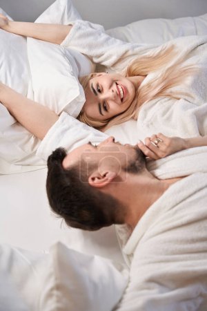 Foto de Feliz recién casados se despiertan en la suite de luna de miel, la pareja está sentada en una cama cómoda - Imagen libre de derechos