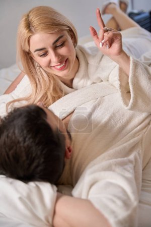 Foto de Los esposos jóvenes se comunican en una cama grande, las personas en albornoces esponjosos - Imagen libre de derechos