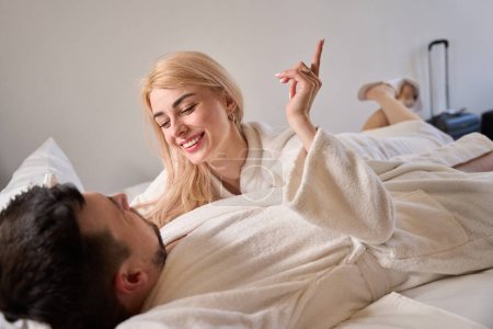 Foto de Feliz hombre y mujer hablando en una cama grande, gente con albornoces esponjosos - Imagen libre de derechos