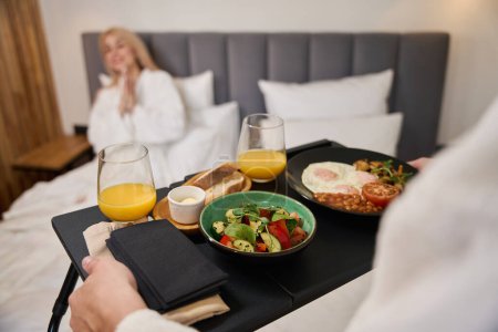 Téléchargez les photos : Mari attentionné apporte un plateau de petit déjeuner au lit, le repas est servi pour deux - en image libre de droit