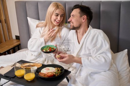 Téléchargez les photos : Homme et femme prennent le petit déjeuner ensemble dans une chambre d'hôtel confortable, ils sont situés dans une chambre confortable - en image libre de droit