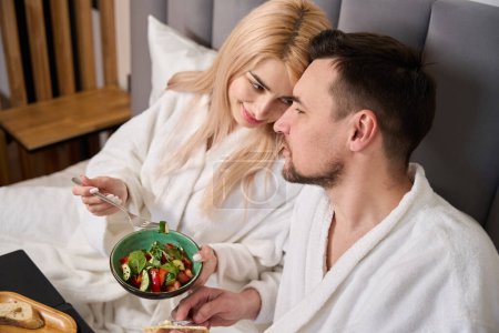 Foto de Linda rubia y su marido están desayunando en una cómoda habitación de hotel, que se encuentran en un acogedor dormitorio - Imagen libre de derechos