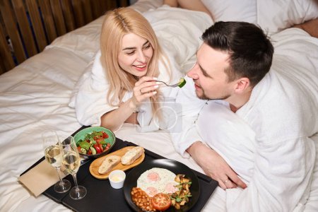 Foto de Pareja joven enamorada se comunica durante el desayuno en la cama, hay dos copas de champán en una bandeja - Imagen libre de derechos