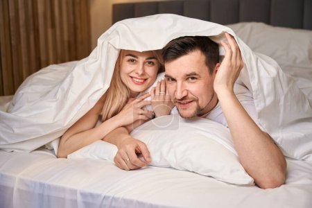 Photo for Young couple is comfortably settled in a honeymoon room, they are lying on a large bed - Royalty Free Image