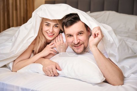 Photo for Newlyweds are comfortably settled in the honeymoon suite, they are lying on a large bed - Royalty Free Image