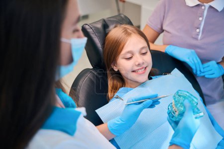 Foto de Higienista dental se comunica durante la consulta con un paciente joven, el médico tiene un modelo de la dentición en sus manos - Imagen libre de derechos