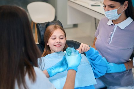 Foto de Dentista demuestra un modelo de una dentición a un paciente joven, con un joven asistente cerca - Imagen libre de derechos
