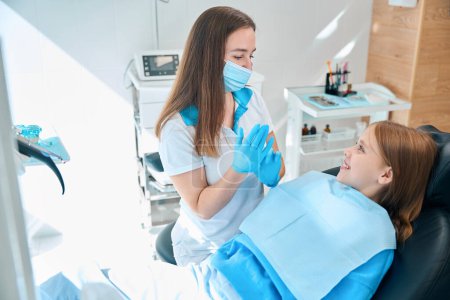 Foto de Adolescente en una silla dental en una recepción de una mujer ortodoncista, un médico con una máscara protectora y guantes - Imagen libre de derechos