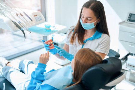 Photo for Specialist in a dental clinic teaches a child oral hygiene using a dummy jaw - Royalty Free Image