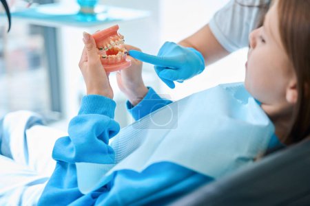 Photo for Dentist hygienist in protective gloves teaches a child oral hygiene using a jaw dummy - Royalty Free Image