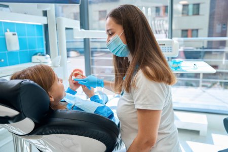 Woman in a dental clinic teaches a child oral hygiene using a dummy jaw