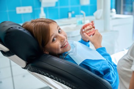 Foto de Adolescente en una recepción en un ortodoncista, ella tiene un modelo de mandíbulas en sus manos - Imagen libre de derechos