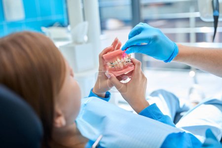 Kieferorthopäde bringt dem Kind bei, die Mundhöhle zu pflegen, wenn es eine Zahnspange trägt, der Arzt benutzt das Maul des Kiefers
