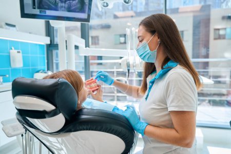 Foto de Dentista y un paciente joven están examinando un modelo de mandíbulas, un médico con una máscara protectora - Imagen libre de derechos