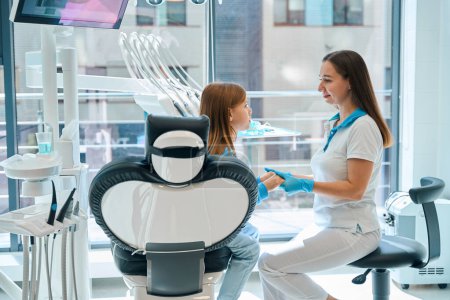 Photo for Female dentist communicates with a young patient in a dental office, the doctor holds the girls hands - Royalty Free Image
