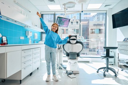 Téléchargez les photos : Fille heureuse dans un bureau dentaire moderne, la chambre est propre et lumineuse - en image libre de droit