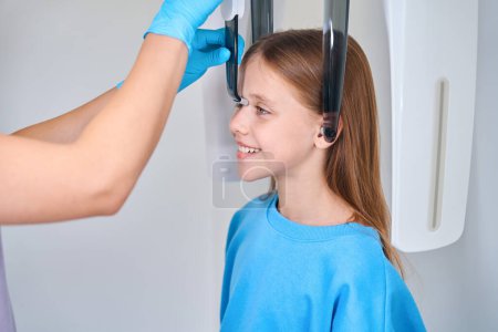 Foto de Trabajador de la salud arregla la cabeza de una niña para una radiografía dental, una mujer que usa guantes protectores - Imagen libre de derechos