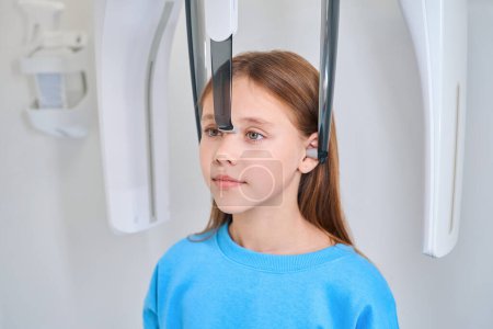 Téléchargez les photos : Une jeune patiente est retenue pour une radiographie dentaire à l'aide d'un équipement moderne - en image libre de droit