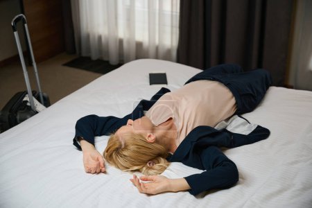 Téléchargez les photos : Femme d'affaires fatiguée couchée sur un lit confortable dans sa suite le matin - en image libre de droit