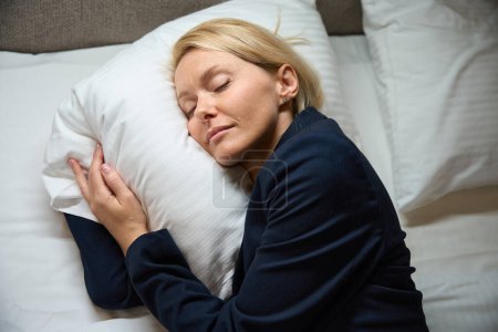 Foto de Mujer de negocios agotada en chaqueta de traje durmiendo en almohada suave en cama cómoda en la recámara - Imagen libre de derechos