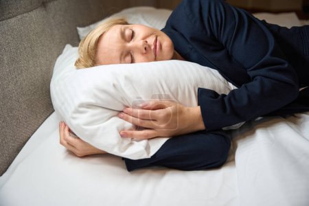 Foto de Mujer emprendedora cansada en traje chaqueta siesta sobre almohada suave en acogedora cama en el dormitorio - Imagen libre de derechos