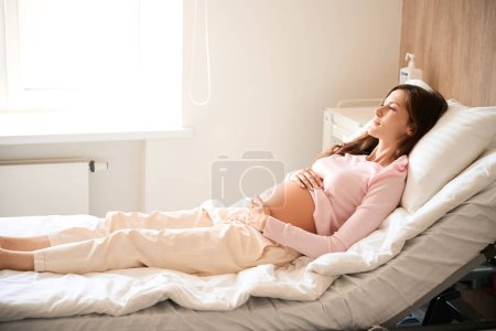 Foto de Hermosa paciente femenina se acuesta en la cama en la sala de hospital antes del parto - Imagen libre de derechos