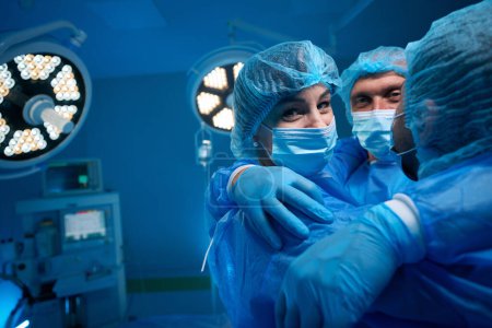 Téléchargez les photos : Équipe chirurgicale réussie câlins dans le théâtre de chirurgie célébrant le travail réussi - en image libre de droit