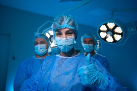 Téléchargez les photos : Chirurgiens professionnels dans le bloc opératoire de l'hôpital après l'opération réussie médecin montrant pouce vers le haut - en image libre de droit